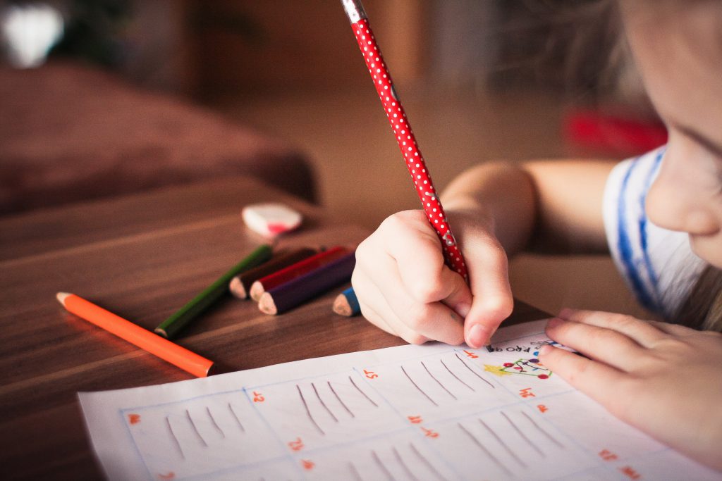 A young girl draws on a piece of paper with a pencil other colored pencils nearby. This could represent a child participating in a test. If you have questions about your child or the signs of autism, contact us for autism testing in Wesley Chapel, FL. An autism evaluation can help you better provide for your child's needs.