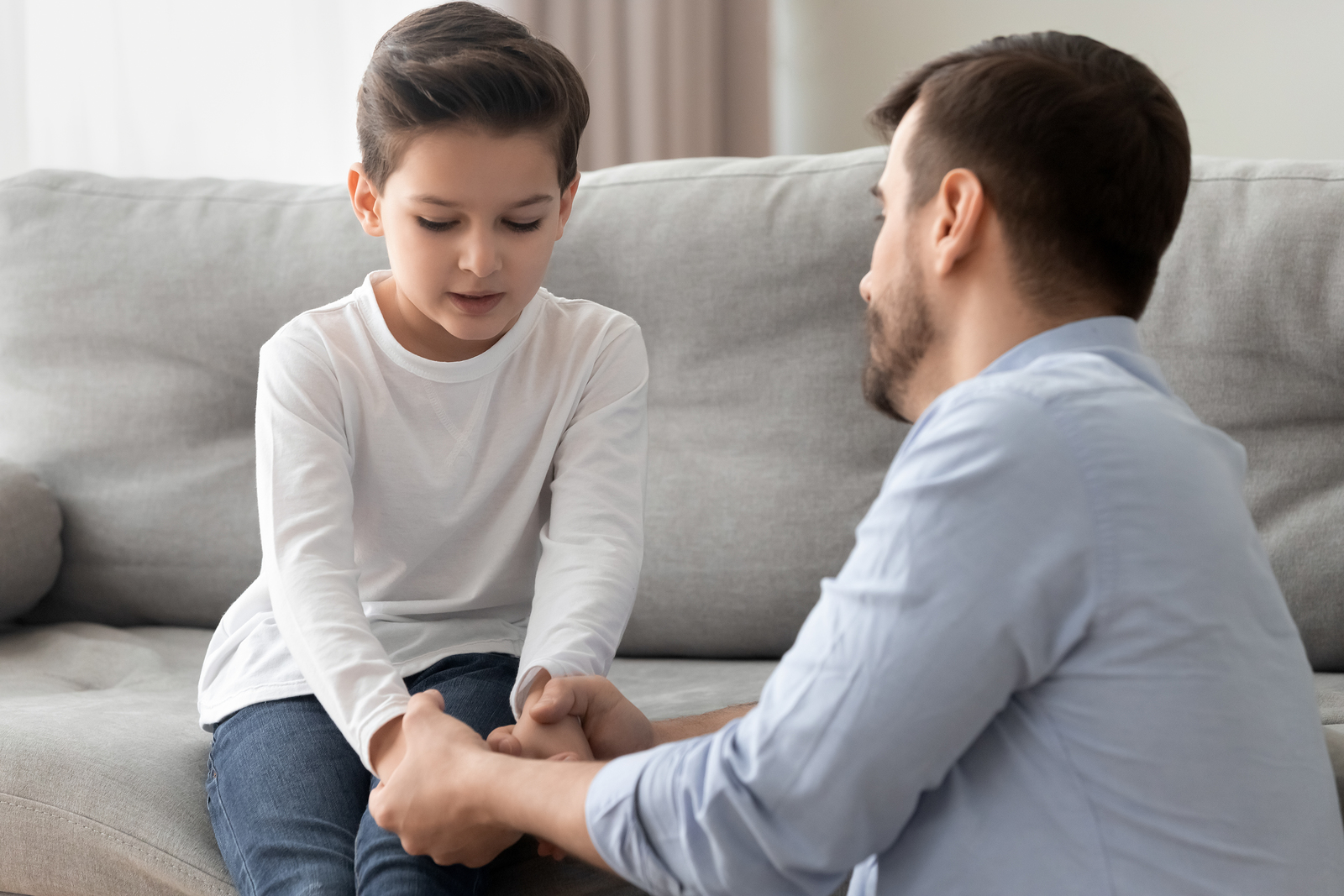 A worried father kneels to reassure his son on the couch. This could represent the support adhd testing offers for children with ADHD and their families. Contact us to learn about an ADHD test for children and ADHD testing near Tampa, FL.  